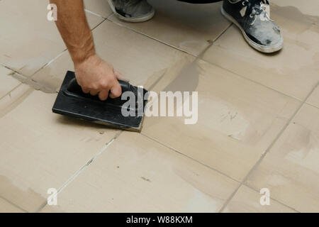 Lavoratore mettendo fugue su piastrelle sul pavimento nel corridoio. Sigillatura delle fughe di piastrelle ceramiche, close up Foto Stock