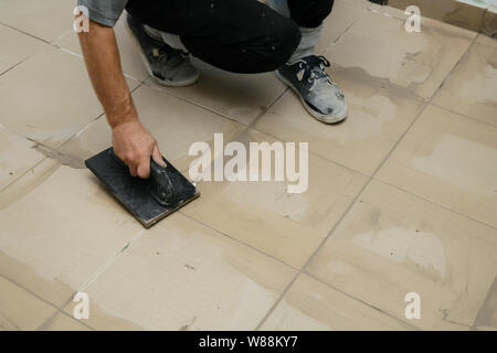 Lavoratore mettendo fugue su piastrelle sul pavimento nel corridoio. Sigillatura delle fughe di piastrelle ceramiche, close up Foto Stock