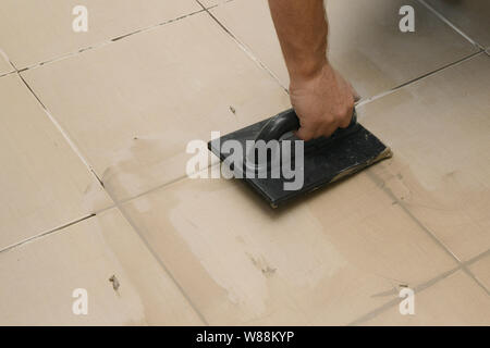 Lavoratore mettendo fugue su piastrelle sul pavimento nel corridoio. Sigillatura delle fughe di piastrelle ceramiche, close up Foto Stock