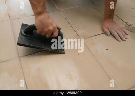 Lavoratore mettendo fugue su piastrelle sul pavimento nel corridoio. Sigillatura delle fughe di piastrelle ceramiche, close up Foto Stock