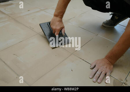 Lavoratore mettendo fugue su piastrelle sul pavimento nel corridoio. Sigillatura delle fughe di piastrelle ceramiche, close up Foto Stock