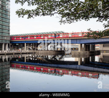 Un treno a West India Quay DLR station di Londra, con riflessione in acqua Foto Stock