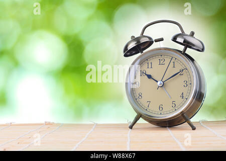 Larm orologio su legno con verdi sfocate bokeh in background. Concetto di tempo Foto Stock