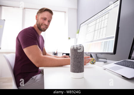 Imprenditore sorridente utilizzando Assistente vocale in ufficio Foto Stock