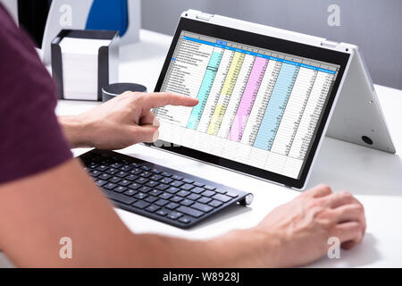 Close-up di un imprenditore il canto esaminando un foglio di calcolo sul computer portatile in ufficio Foto Stock