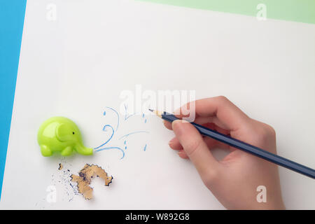 Carino affilatore per bambini sotto forma di elefante, mano con matita blu che disegna un getto d'acqua e una matita limatura. Disposizione piatta Foto Stock