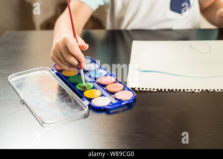 Dettaglio di un bambino con le mani in mano tenendo un pennello e pittura con acquarello su carta. Concetti di infanzia e il ritorno a scuola. Foto Stock