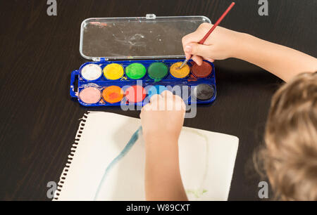 Dettaglio di un bambino con le mani in mano tenendo un pennello e pittura con acquarello su carta. Concetti di infanzia e il ritorno a scuola. Foto Stock