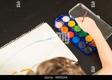 Dettaglio di un bambino con le mani in mano tenendo un pennello e pittura con acquarello su carta. Concetti di infanzia e il ritorno a scuola. Foto Stock