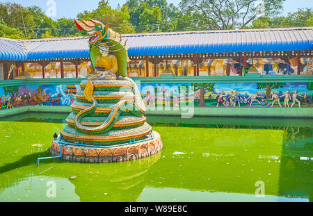 MONYWA, MYANMAR - 22 febbraio 2018: il colorato Naga-Raja statua del Buddha in mezzo il piccolo laghetto nella Pagoda Thanboddhay complesso, circondato da sollievo reli Foto Stock