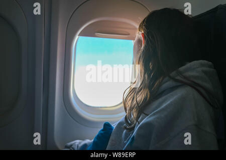 Ragazza a guardare fuori dalla finestra di aereo in volo mentre si è in viaggio Foto Stock