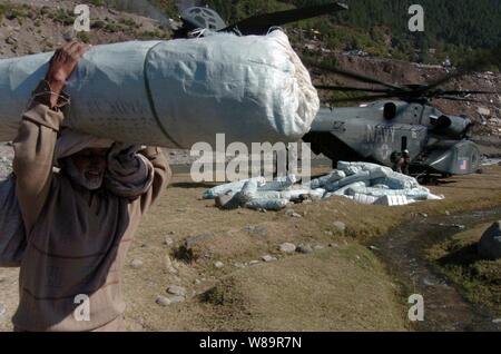 Un anziano uomo pakistano porta una tenda lontano dalla U.S. Navy MH-53 mare Dragon elicottero in Balikot, in Pakistan, il Ott 19, 2005. Il Dipartimento della difesa è che partecipano alla multinazionale di sforzo per fornire assistenza umanitaria e assistenza al Pakistan e parti dell India e in Afghanistan a seguito di un terremoto devastante. Il mare Dragon è attaccato alla miniera di elicottero contromisure Squadron 15 della Naval Air Station, Norfolk, Virginia Foto Stock