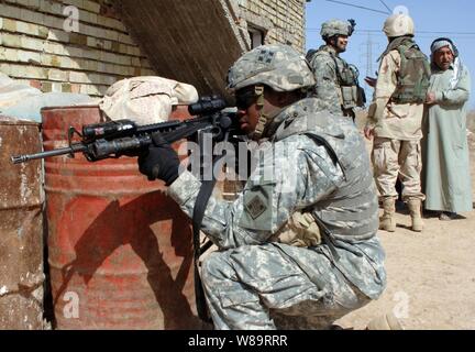 Pfc dell'esercito. Jonathan Dixon (in primo piano) fornisce la protezione del perimetro mentre il personale Sgt. Gabriel Monreal e il suo traduttore condurre un colloquio locale con un uomo iracheno durante una pattuglia di routine nei pressi di Camp Taji, Iraq, il 13 marzo 2006. Dixon e Monreal sono attaccati alla società alfa, 1° Battaglione, 66reggimento blindato. Foto Stock