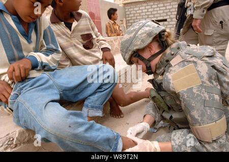Stati Uniti Pfc dell'esercito. Boschi Corione pulisce una ferita aperta su un bambino iracheno è la gamba al di fuori del Al-Nasar Welsalem stazione di polizia a Baghdad, Iraq, il 4 maggio 2006. Boschi è il trattamento della gamba boyís durante un quartiere misto patrol con soldati dell'esercito iracheno. Foto Stock