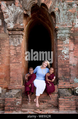 Un Caucasian turista femminile e due buddista birmano novizio monaci in un antico tempio rideva di telecamera in Bagan Myanmar e turistico è rilasciato. Foto Stock