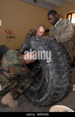 Stati Uniti Army Sgt. Raymond Averesch (sinistra), PFC. Curtis Lacher (centro) e SPC. Cedrick Griffin, con la forza militare di transizione e di formazione del team, assemblare una ruota per una miniera-resistenti, imboscata-veicolo protetto in Kadhimiya, Iraq, nel febbraio 23, 2009. Foto Stock