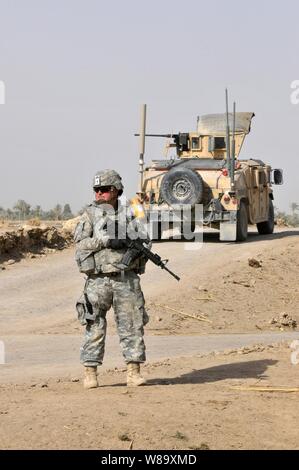 Un U.S. Soldato dell'esercito con il primo plotone, Comanche truppa, 1° Stormo, 150° reggimento di cavalleria, trentesimo Heavy Brigade Combat Team, 1a divisione di cavalleria fornisce la sicurezza come soldati iracheni con 1° Company, 3° Battaglione, XXIII brigata, xvii divisione irachena di armi condurre ricerche cache attraverso campi aperti nell'area Radwaniyah fuori Baghdad, Iraq, il 18 luglio 2009. Foto Stock