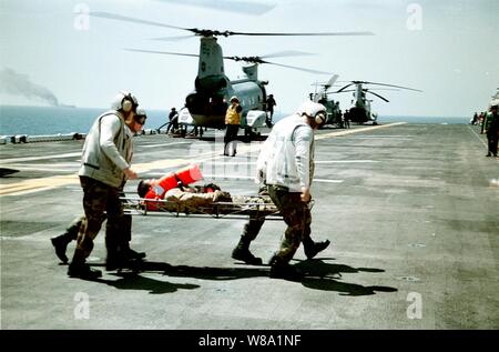 Stati Uniti Marines da combattimento Cargo rush plotone di un marinaio ferito dalla nave mercantile Seal-Land Mariner, visto variopinte sullo sfondo per il dipartimento di scienze mediche a bordo della U.S. Navy Amphibious Assault nave USS Wasp (LHD 1) nel Mare Mediterraneo il 18 aprile 1998. Ricerca e salvataggio di membri di equipaggio, elicotteri e un 18-persona alla squadra antincendio da The Wasp ha risposto ad una emergenza chiamata di emergenza dalla nave mercantile nel Mare Mediterraneo, a circa 85 miglia ad ovest di Creta. Un U.S. Navy CH-46 Sea Knight elicottero aria-sollevato due della nave mercantile membri di equipaggio per il Wasp Foto Stock