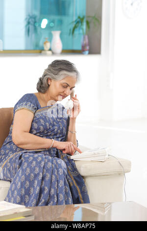 Donna senior di comporre su un telefono di rete fissa Foto Stock