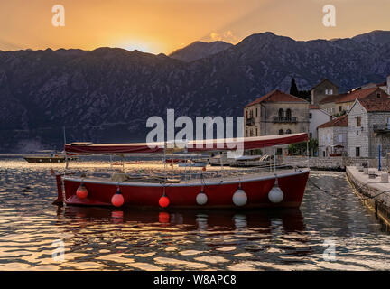 Vista panoramica di una barca ormeggiata in cartolina perfetta città di Perast nella Baia di Kotor con il sole che tramonta dietro alle montagne in estate, Montenegro Foto Stock