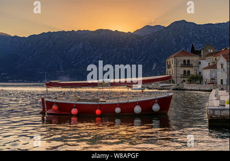 Vista panoramica di una barca ormeggiata in cartolina perfetta città di Perast nella Baia di Kotor con il sole che tramonta dietro alle montagne in estate, Montenegro Foto Stock