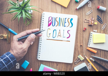 Obiettivi BUSUNESS messaggio maschio con la scrittura a mano su notepad carta sul tavolo di legno e delle forniture per ufficio.concetti commerciali.piatto design dei laici Foto Stock