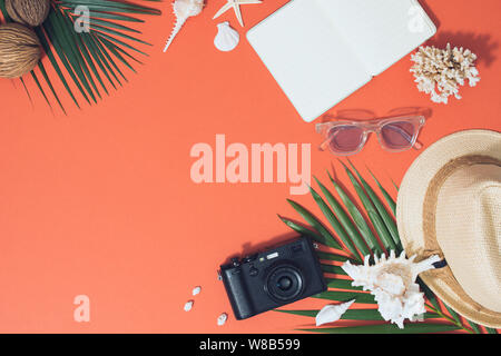 Colorate le vacanze estive moda lay piatto - cappello di paglia, macchina fotografica, occhiali da sole, mare, conchiglie luminose su sfondo arancione Foto Stock