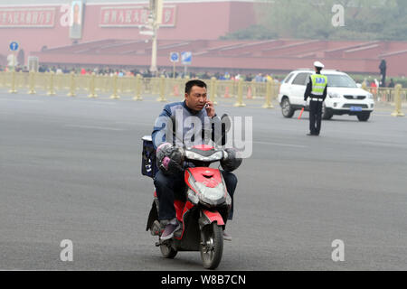 --FILE--un ciclista cinese parlando sul suo telefono mobile scorre una bicicletta elettrica attraverso la piazza Tiananmen a Pechino, in Cina, il 6 aprile 2016. La growin Foto Stock