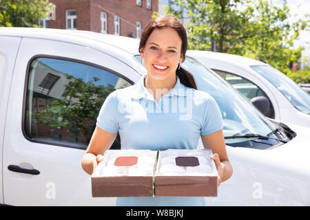 Sorridente donna consegna le scatole di contenimento delle ciambelle in piedi nella parte anteriore della macchina Foto Stock