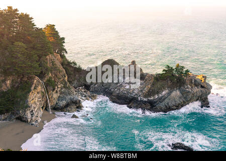 Il caldo lavaggio della luce del mattino sopra le cascate McWay lungo la costa di Big sur in California. Foto Stock