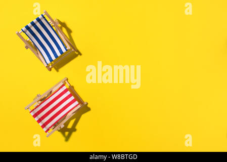 Due sedie a sdraio con disco shadow, monstera e foglie di palmo sulla carta gialla sfondo. Appartamento di laici e di spazio copia. Viaggio estivo Concetto di vacanza. Composizione minima. Foto Stock