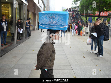 Nove-anno-vecchio ragazzo Ye Jianjun gioca con una scatola di cartone che egli utilizza a mendicare per denaro sulla testa dopo una prestazione su una strada nella città di Changsha, Cina centrale' Foto Stock