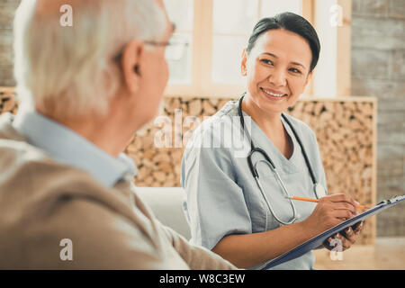Piuttosto medico con lo stetoscopio sul suo collo elencando i reclami Foto Stock