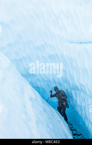 Allegra di arrampicata su ghiaccio a piedi di guida attraverso stretti canyon inclinata sul ghiacciaio Matanuska. Egli cammina attraverso un fiume poco profondo che tagliare il canyon da th Foto Stock