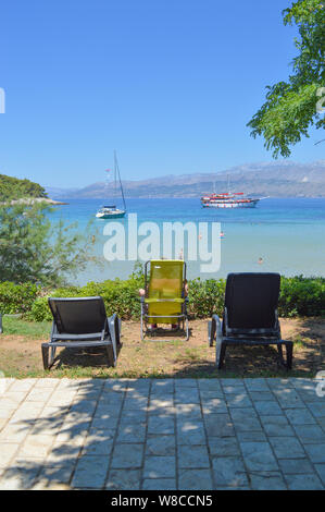 Scena di spiaggia con sedie a sdraio, acqua cristallina e le barche a vela, Lovrečina beach, isola di Brac, Croazia Foto Stock