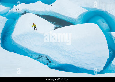 Sul ghiacciaio Matanuska in Alaska, un giovane uomo cammina il crinale di una pinna di ghiaccio isola in un lago glaciale. Foto Stock