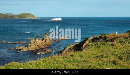 In una tranquilla giornata invernale, il ferry Aratere lascia il porto di Wellington, legato per Picton nell'Isola del Sud, guardato da due escursionisti sul punto Dorset Foto Stock