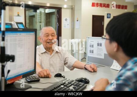 Il 97-anno-vecchio magazzino cinese investor Shi Kunsen, sinistra, colloqui con un dipendente di uno stock brokerage house di Hangzhou, a est della Cina di Zhejiang provinc Foto Stock
