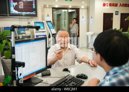 Il 97-anno-vecchio magazzino cinese investor Shi Kunsen, sinistra, colloqui con un dipendente di uno stock brokerage house di Hangzhou, a est della Cina di Zhejiang provinc Foto Stock