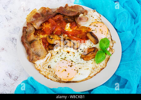 Uova fritte con pancetta, i pomodori e i funghi su sfondo bianco. Vista superiore Foto Stock
