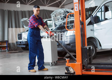 Meccanico femmina in rosso e blu uniforme funziona con il grande bianco carrello per il passato un paio di ore. Foto Stock