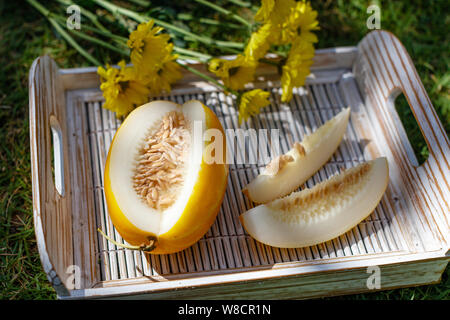 Tagliare giallo melone orientali (Coreano melone) su un bianco vassoio in legno Crisantemo giallo sullo sfondo. Foto Stock