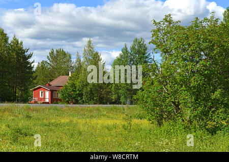 Rosso casa di legno nella foresta vicino a strada. La Lapponia finlandese Foto Stock
