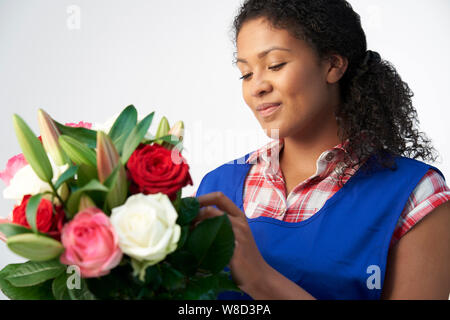 Studio shot di fiorista femmina disponendo bouquet di Lillies e rose contro uno sfondo bianco Foto Stock