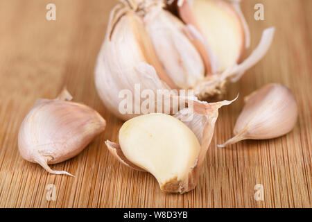 Una testa di aglio, parecchi chiodi di garofano di aglio sbucciato e uno spicchio sbucciato su uno sfondo di legno. Foto Stock