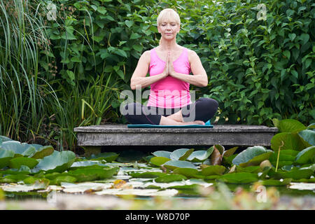 Donna matura in posizione di Yoga sul pontile in legno sul Lago di Garda Foto Stock