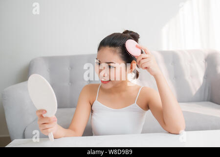 Giovane donna asiatica la pettinatura dei capelli e cercando in specchio Foto Stock