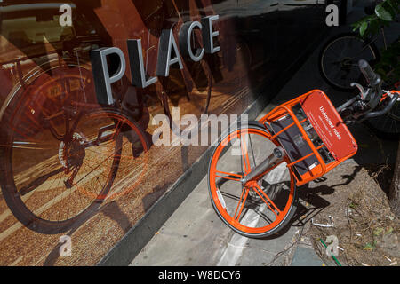 Un noleggio Mobike appoggia contro un albero accanto ad una illustrazione di un'utopia in bicicletta a un nuovo sviluppo chiamato una corona posto su Sun Street vicino alla stazione di Liverpool Street nella città di Londra, capitale del distretto finanziario - aka il miglio quadrato il 8 agosto, a Londra, in Inghilterra. Foto Stock