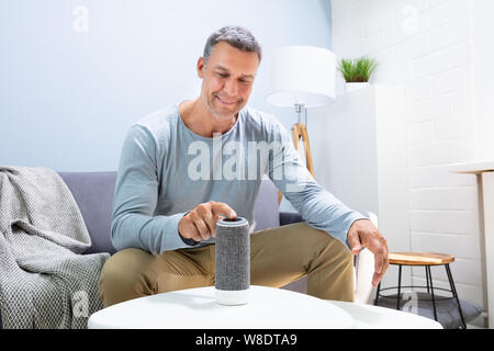 L'uomo premendo il pulsante su altoparlante wireless a casa Foto Stock