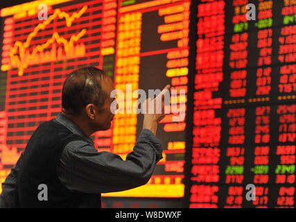 Un investitore cinese sorride come egli guarda gli indici azionari e i prezzi delle azioni (rosso per il prezzo in aumento e verde per la caduta dei prezzi) in corrispondenza di un magazzino di ho di brokeraggio Foto Stock